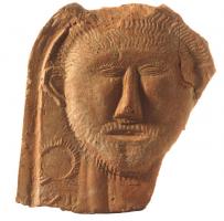 ANT-4033 - Antéfixe: tête masculineterre cuiteTPQ : 1 - TAQ : 100Antéfixe moulée, à sommet arrondie, figurant un buste d'homme moustachu et barbu, les cheveux courts, dans un style schématique; sur le côté gauche, chiffre avec une couronne.