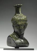 BLS-4025 - Balsamaire en forme d'hermèsbronzeTPQ : 1 - TAQ : 100Balsamaire en forme d'Hermès juvénile, la tête tournée vers la droite, les cheveux coiffés en mèches courtes et serrés par un diadème ; les yeux sont incrustés d'argent. Le vase a été obtenu très simplement en ajoutant un col cylindrique au sommet du crâne.