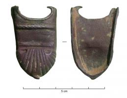 BOF-9009 - Bouterolle de fourreaubronzeBouterolle de fourreau d'épée de forme trapézoïdale ; base arrondie munie d'un petit bouton ; deux appendices latéraux en partie supérieure ; décor mouluré comprenant deux cordons horizontaux, l'un en partie supérieure, l'autre en partie médiane ; motif en forme de coquillage couvrant la moitié inférieure. 