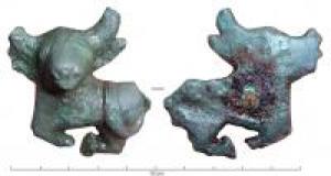 CLD-3003 - Applique zoomorphebronzeApplique (bas-relief) en forme de taureau couché, la queue revenant vers le dos, la tête hypertrophiée, traitée dans le style celtique; sous le corps, les pattes sont repliées l'une vers l'autre. Au revers, tige de fixation en fer.