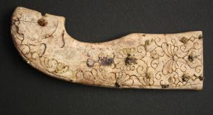 EPE-3034 - Poignée de machairaivoireObjet en forme de crosse, avec placage circulaire fixé par un rivet de cuivre ou de bronze; décor gravé d'inspiration végétale, avec feuilles de lierre, palmettes etc. L'autre extrémité est complète.
