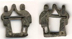 FER-7029 - Fermail figuratifbronzeFermail dont l'anneau est constitué de deux personnages d'un couple reposant sur un trait de sol, et levant deux mains qui se joignent.