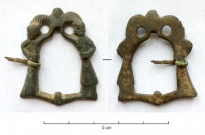 FER-7033 - Fermail figuratifbronzeFermail dont l'anneau est constitué de deux personnages symétriques sur un trait de sol, et levant deux mains rejoignant une colombe aux ailes déployées.