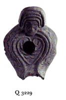 LMP-41406 - Lampe byzantine Tête terre cuiteLampe à bec long à canal; corps massif; anse plastique en forme de tête humaine. Médaillon décoré d'un motif linéaire cordiforme.