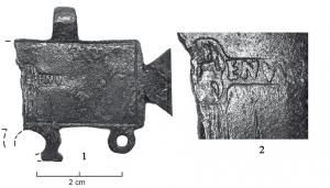 PDH-4175 - Pendant de harnais en tabula ansatabronzePendant en forme de tabula ansata, avec suspensions sommitales centrées et trois anneaux à la base pour y suspendre des pendants. La surface porte une estampille centrée, répartie de part et d'autre d'un motif figuré également estampé.