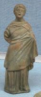 STE-3004 - Statuette : personnage fémininterre cuiteFigurine moulée représentant une femme drapée (chiton et himation), sur une base plate; la main gauche passée sur le chiton tend le vêtement par dessous, la main droite est dans le dos.