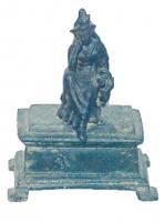 STE-4156 - Statuette : femmebronzeStatuette en bronze présentant une femme assise sur un rocher, personnification de la Cilicie? Vêtue d'un long manteau, le coude repose sur la cuisse droite relevée et les doigts posés pensivement sur la joue. Elle porte une coiffure surmontée d'une plume ou d'une feuille verticale ; la main gauche posée sur la jambe correspondante tenait sans doute un objet, détaché. L'ensemble est fixé sur un socle rectangulaire qui ne semble pas être d'origine.