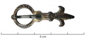 BOH-9002 - Boucle d'éperonbronzeBoucle rigide, dorée, dont le corps percé pour l'articulation d'un ardillon se prolonge par une fleur de lis percée pour offrir une solide fixation rivetée ; l'anneau pourvu d'un repos d'ardillon en gouttière est orné de rinceaux gravés.