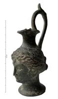 CRU-9004 - Faux : cruche céphalomorphebronzeCruche ou œnochoé en forme de tête   féminine, de style grec classique, avec une anse surélevée ornée d'un poucier sommital.