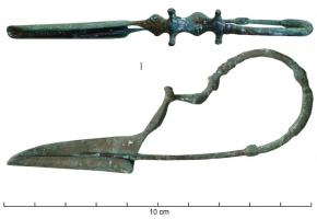 FIB-2079 - Fibule a dragobronzeFibule sans ressort (l'arc se prolonge directement par l'ardillon), à long pied triangulaire plein ; au contact du pied, l'arc est orné de deux écrasements ovales suivis d'une paire de 
