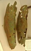 JMB-2002 - JambièrebronzeJambière en tôle, de forme anatomique, épousant le genou et enveloppant le mollet jusqu'à la cheville. Le contour de la rotule et le muscle du mollet peuvent être soulignés par des sillons ou des reliefs.