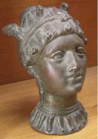 BLS-3004 - Balsamaire en forme de tête fémininebronzeBalsamaire en forme de tête féminine, les traits classiques, les cheveux tirés en arrière et retenus par un bandeau; le col du vase placé au sommet du crâne est équipé de deux bél!ères coulées.