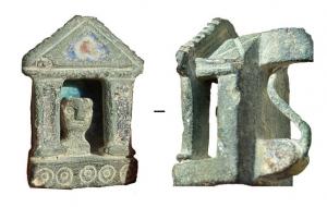 FIB-41753 - Fibule architecturale : Temple avec statuebronzeFibule composée d'un arrière plan rectangulaire émaillé, avec une articulation à deux plaquettes; au premier plan on trouve un temple à deux colonnes sur socle, soutenant un fronton émaillé qui protège un buste d'idole.
