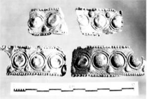 IND-4236 - Bandeau indéterminébronzeMince feuille de bronze décorée au repoussé : sur les bords, pseudo granulations, au centre, frise de bossettes définies par des cercles et surmontées d'arcs de cercles, d'où pendent des motifs piriformes. L'un des six fragments conservés présente les restes d'une soudure à l'étain.