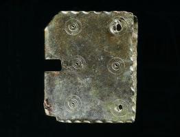 PLB-4018 - Plaque-boucle en tôlebronzePlaque-boucle à plaque quadrangulaire en tôle, repliée sur elle-même et échancrée pour la boucle et l'ardillon; décor de cercles concentriques (4 ou 6) ; rivets de fixation.