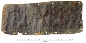 PLV-4007 - Plaquette votivebronzePlaque en tôle, comportant deux fois la même scène estampée à partir d'un bloc (sans doute en bronze) rectangulaire à sommet arrondi : au centre, un personnage à cheval se dirige vers la droite, avec à sa gauche Hermès (caducée) et à sa droite une figure ailée (Lare ? Victoire ?), avec à ses pieds un serpent; au-dessus, deux bustes radiés entourés d'un aigle, croissant de lune et autres symboles; des arbres au tronc noueux, chargés de fruits, ont été ajoutés au repoussé de part et d'autre de la double scène, et le pourtour percé témoigne d'une fixation clouée.