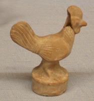 STE-3005 - Statuette zoomorphe : coqterre cuiteFigurine moulée représentant un coq, debout sur une base cylindrique; les détails des plumes des ailes et de laqueue sont indiqués par des incisions.