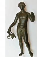 STE-4476 - Statuette : BacchusbronzeTPQ : 1 - TAQ : 300Bacchus sous la forme d'un jeune nu, en position déhanchée, tenant à droite, à bout de bras,  une amphore à panse godronnée, la main droite relevée et sans doute appuyée sur un thyrse.