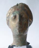 STE-4553 - Statue : tête fémininebronzeTête de statue féminine, brisée au niveau du cou. Le visage a été abîmé par la corrosion. La coiffure est composée d’une raie au sommet du crâne et de deux bandeaux ondulés qui vont vers l’arrière et qui couvrent les oreilles. La chevelure s’interrompt au niveau d’une bande utilisée pour ajouter une autre pièce et ainsi compléter la tête de la statue.