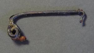 FIB-3028 - Fibule en fer à arc tenduferFibule en fer à ressort bilatéral, 4 spires, corde externe et griffe ; arc très tendu, de section filiforme généralement ronde, parfois carrée, avec porte-ardillon de type inconnu.