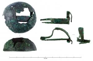 FIB-31008 - Fibule à timbalebronzeTPQ : -500 - TAQ : -400Fibule à long ressort bilatéral, corde externe, arc rubanné et pied inorné, recouverte d'une large cupule à bord décoré d'incisions 