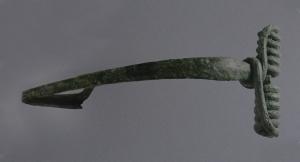 FIB-3981 - Fibule de type La Tène C2bronzeFibule à arc coulé et tendu, de section losangique aplatie; ressort long à corde enroulée autour de l'arc; pied droit, porte-ardillon triangulaire ajouré.

