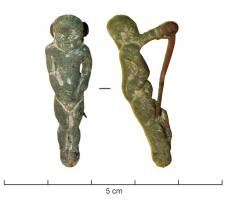 FIB-41168 - Fibule anthropomorphebronzeFibule anthropomorphe, en forme de jeune garçon, nu, le crâne rasé, les mains posées sur le ventre; le corps est potelé et la tête, ronde, disproportionnée par rapport au corps.