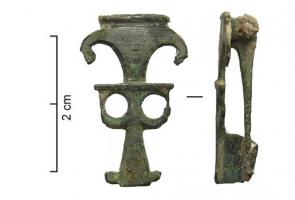 FIB-4666 - FibulebronzeBroche plate, étamée, avec une superposition de motifs découpés au-dessus d'un pied triangulaire, à protubérances latérales à l'extrémité; paire d'ajours circulaires; protubérances latérales en forme de cornes (ou de têtes zoomorphes?).