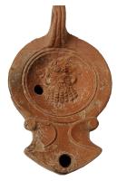 LMP-42676 - Lampe Loeschcke I : Tête de Silèneterre cuiteLampe ronde à large bec en enclume à volutes. Médaillon concave orné d'une tête de Silène, oreilles animales et large barbe frisée ; épaule large plate ; anse moulée et percée à l’arrière, cannelée de deux sillons ; base plate définie par un sillon circulaire et portant une marque gravée : L.MVN.SVC.