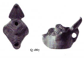 LMP-4841 - Lampe plastique Masque PROKAGOUterre cuiteLampe plastique en forme de masque grotesque. Anse triangulaire décorée de trois pétales. Marque POOKAGOU en lettres grecques incisée.