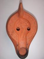 LMP-5256 - Lampe Hayes II : Eveterre cuiteLampe africaine tardive classique. Médaillon orné d'une femme se tenant les cheveux : Eve? Epaule ornée de motifs géométriques. Argile orange, engobe orange. Anse à l'arrière.