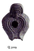 LMP-6047 - Lampe byzantine Tête terre cuiteLampe à bec long à canal; corps massif; anse plastique en forme de tête humaine. Médaillon décoré d'un motif linéaire cordiforme.