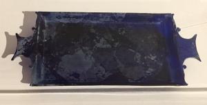 PLA-4045 - Plateau mouléverrePlateau rectangulaire moulé, généralement en verre coloré (vert foncé, bleu, violet, brun...), pourvu d'un bord oblique et de deux anses latérales rectangulaires à bords concaves pour la préhension.
