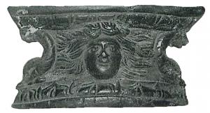 SIT-4051 - SupportbronzeSupport de situle en large plaque incurvée, ornée de reliefs, avec la base et le sommet moulurés : au centre une tête humaine, deux dauphins têtes en bas soutiennent les côtés échancrés.