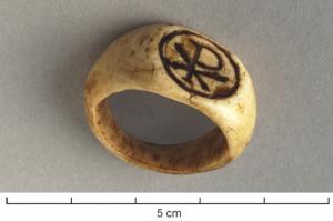 BAG-4185 - Bague avec chrismeosBague taillée dans une diaphyse, avec un anneau qui s'élargit progressivement pour forme un important chaton plat et ovale, parfois nettement séparé du jonc, gravé d'un chrisme dans un cadre.