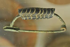 FIB-2558 - Fibule à arc en verrebronze, verreFibule à arc filiforme, orné d'une perle cylindrique en verre, à décor de plumes.