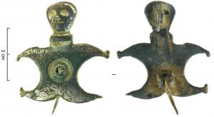 FIB-4513 - Fibule géométrique platebronzeFibule plate étamée, composée de 2 peltes accolées dont les branches figurent les membres d'un personnage, surmontés d'une tête humaine de face ; au centre, un cercle en creux percé d'un trou. 