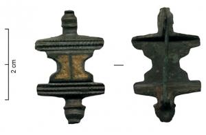 FIB-4978 - Fibule symétrique émailléebronzeFibule symétrique à partie centrale en forme de sablier, creusée et entièrement émaillée; la symétrie est assurée par 2 barrettes transversales guillochées, prolongées par des boutons moulurés.
