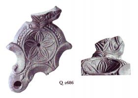LMP-41184 - Lampe Loeschcke III à deux becs : rosetteterre cuiteLampe ronde à double bec à volutes avec terminaison en ogive et pomme de pin entre les volutes. Médaillon orné d'une rosette. Anse plastique triangulaire, fragmentaire avec buste masculin (Sérapis?).