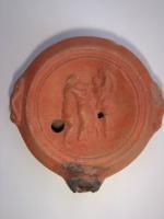 LMP-4437 - Lampe Loeschcke VIII tardive Sarabandeterre cuiteLampe à court bec rond. Disque décoré d'une sarabande : un satyre à gauche enlace une femme, tandis qu'une danseuse joue devant eux, à droite. Argile orange, engobe orange; base plate.