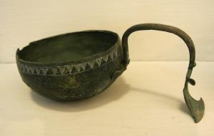 SPL-2004 - Simpulum italique à manche sinusoïdal
bronze
Simpulum à anse rivetée; la vasque hémisphérique est ornée sous le bord d'un décor incisé (triangles hachurés et motif réticulé); l'anse se rattache à la vasque grâce à une applique cruciforme rivetée à l'extérieur du vase; la terminaison de l'anse, sinusoïdale, forme une sorte de palette caractéristique.