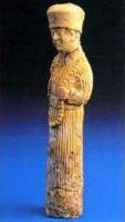 STE-2001 - Statuette : prêtreivoireStatuette d'un personnage en longue robe droite, large ceinture, et coiffé d'un bonnet cylindrique; il tient de la main gauche un collier de grosses perles descendant jusqu'au bassin.