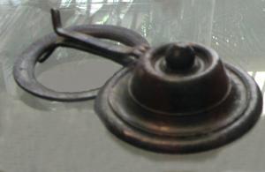 APM-4085 - Applique de meublebronzeApplique circulaire, simplement ornée de moulures concentriques en fort relief, avec ou sans bouton sommital ; revers creux sans autre mode de fixation qu'une fente dans le bord de l'objet, sur laquelle est parfois conservée un crampon replié sur lui-même. Le crampon peut parfois servir aussi à maintenir un anneau articulé qui encadre l'applique.