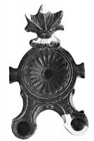 LMP-4031 - Lampe à deux becs et anse plastiqueterre cuiteLampe à deux becs en ogive à volutes latérales; anse plastique en forme de feuille de vigne; deux ailerons latéraux rubannés sortent horizontalement de l'épaule; disque décoré d'une rosette.