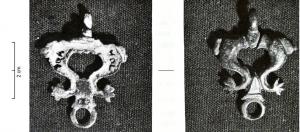 PDH-4141 - Pendant de harnaisbronzePendant de harnais composé de deux deux dauphins opposés par leur bouche ; les queues des animaux se réunissent à la base d'une seconde bélière qui pourrait permettre la fixation d'un élément décoratif.
