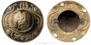 BCE-4002 - Umbo de bouclierbronzeUmbo de parade, en laiton étamé, avec reliefs au repoussé et manipule en fer au revers. Au centre, Minerve corinthienne assise; sur la bande externe, serpents, masques, aigle et fleuron.