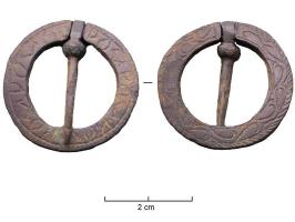 FER-7012 - Fermail inscritbronzeAnneau plat comportant un rétrécissement servant d'axe à un ardillon; décors de volutes incisées sur une face, et d'une inscription de l'autre.