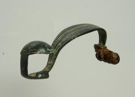 FIB-3561 - Fibule à timbale sur le piedbronzeFibule à timbale sur le pied (parfois bordée d'un filet), l'arc en anse de panier est foliacé et orné d'incisions ; ressort mince à 6 spires et corde interne.