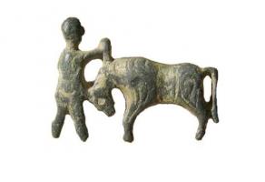 FIB-41678 - Fibule zoomorphe, groupe : bestiarius ?bronzeBroche présentant un personnage debout à gauche, plantant un poignard dans l'encolure d'un taureau tête baissée à droite