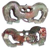FIB-5014 - Fibule zoomorphe : monstre bicéphalebronzeFibule zoomorphe constituée de deux protomes de chevaux adossés; le museau rejoint la patte antérieure pliée. Au revers, bélière avec anneau, sans doute pour une chaînette reliant une paire de fibules semblables.